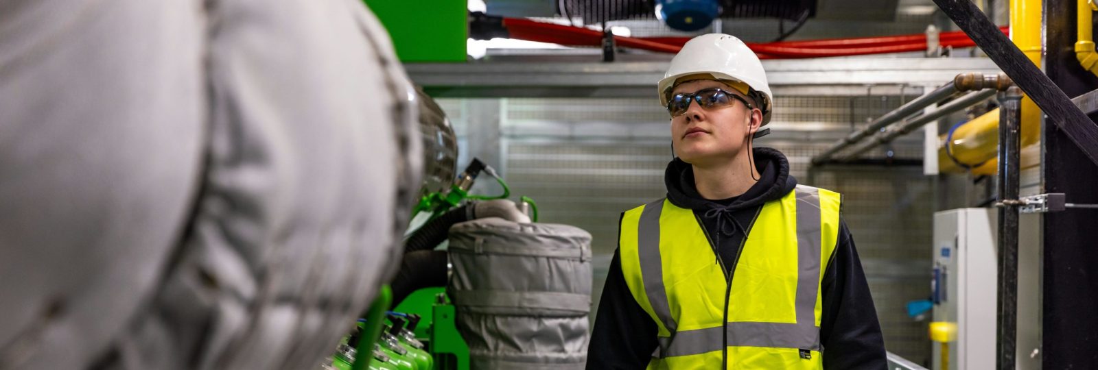 Mann mit Warnweste und Helm in einer Industrieanlage.